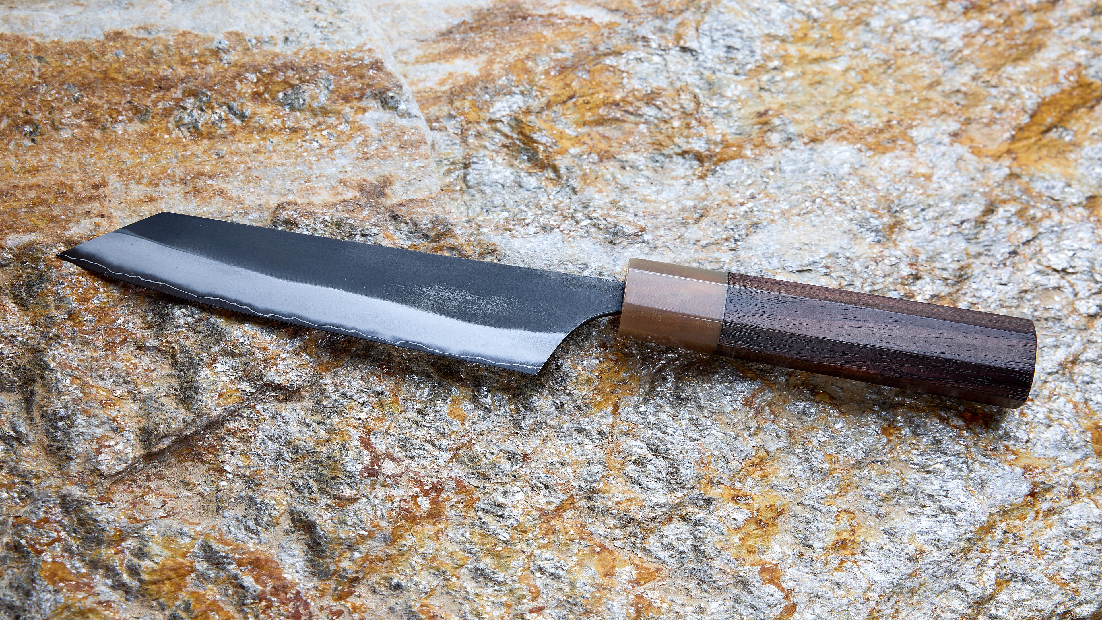 A 135 mm Japanese kiritsuke-style petty knife intended for small, precise cutting tasks such as trimming and slicing on a cutting board. It has an SLD semi-stainless steel core, a dark-finished blade, and a profile combi