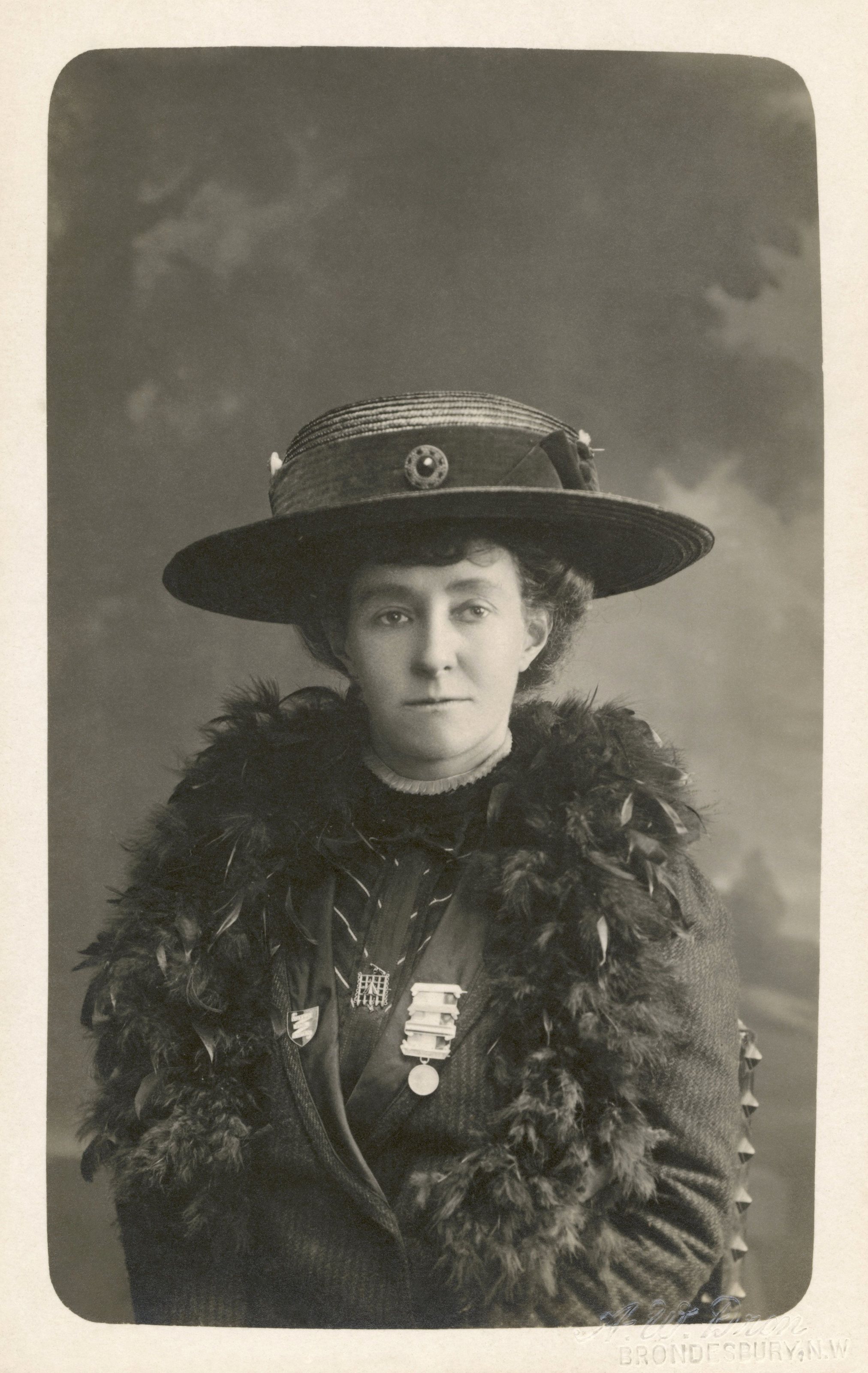 Photo of  Emily Wilding Davison  wearing her  hunger strike medal  and  Holloway brooch . The Mary Evans Picture Library calls this a postcard. 
  Text embossed on image: "A.W. Dron /  Brondesbury , N.W." (N.W. meaning N
