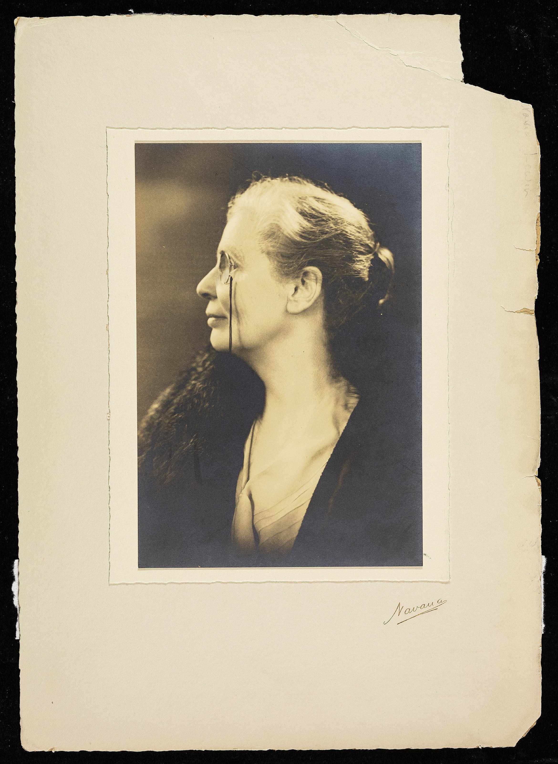 Monochrome studio portrait of Octavia Lewin, head and shoulders, left profile, wearing a monocle, mounted on card.